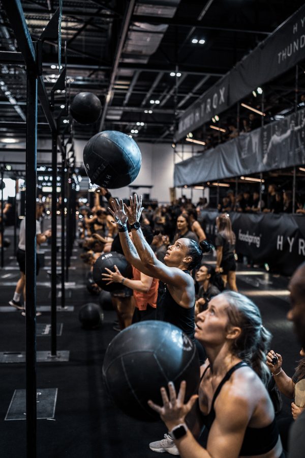 A row of competitors perform the wall ball exercise at a Hyrox event.