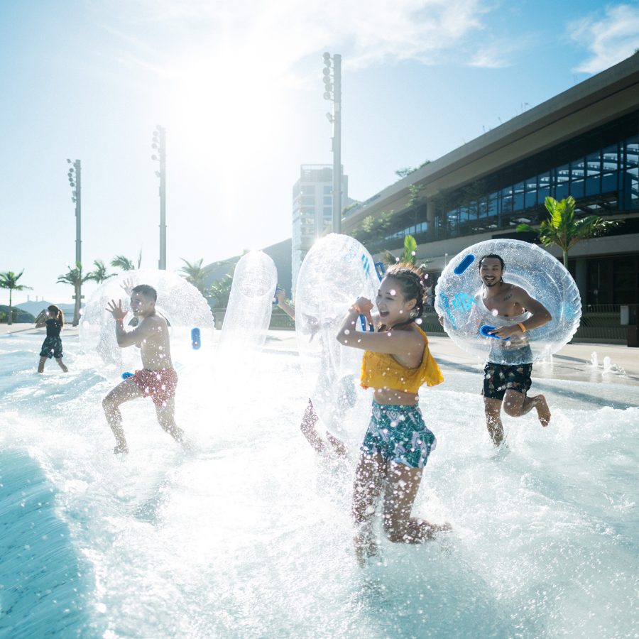 A group of people run into an outdoor pool at Water World Ocean Park while wearing inner tubes. 