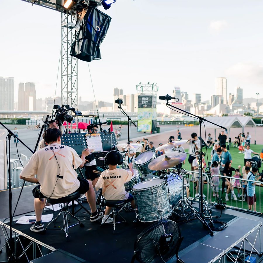 Performers are onstage behind a drum set looking over an audience at SummerFest Hong Kong. 