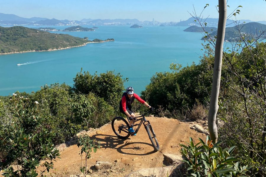 A person riding a bike on a trail with a body of water and mountains in the background.