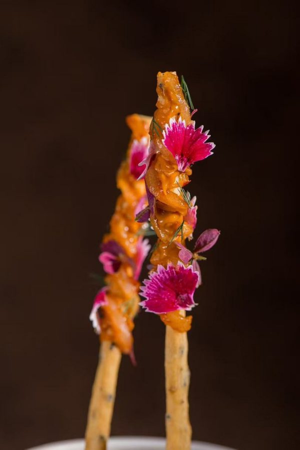 Two skewers are decorated with pink flowers in a dish at Flame Restaurant. 