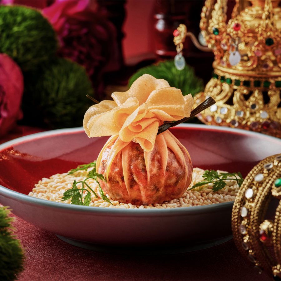 A large dumpling full of fried minced meat is placed on a table adorned with golden jewellery at Queen Cheuk Yuet. 