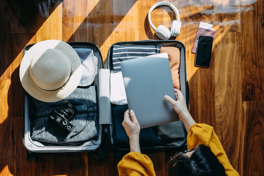 A person packs clothes and other personal belongings into a small suitcase.