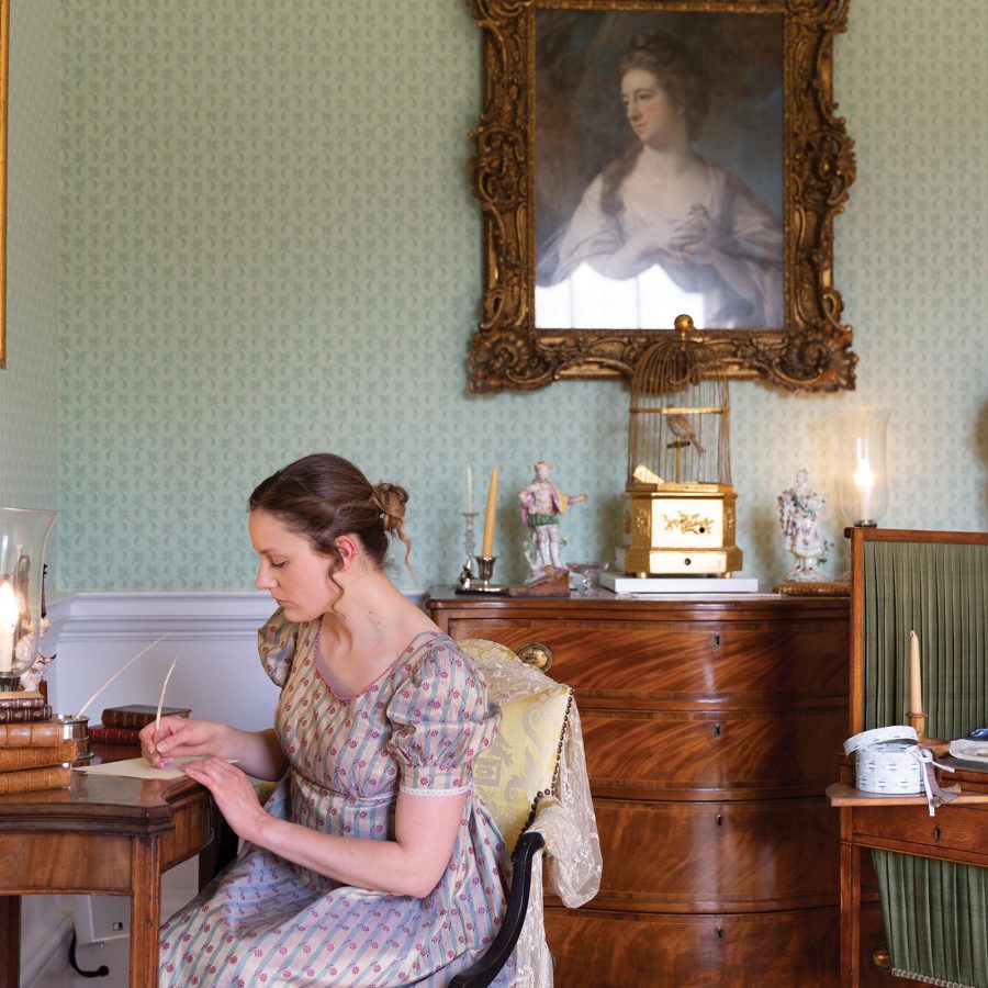 A woman in Regency dress writing at a desk.