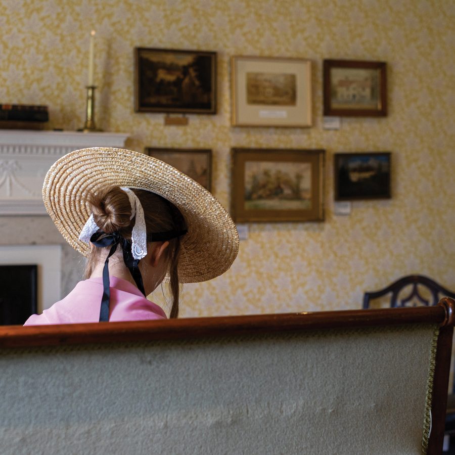 A woman in a hat sitting in a drawing room.