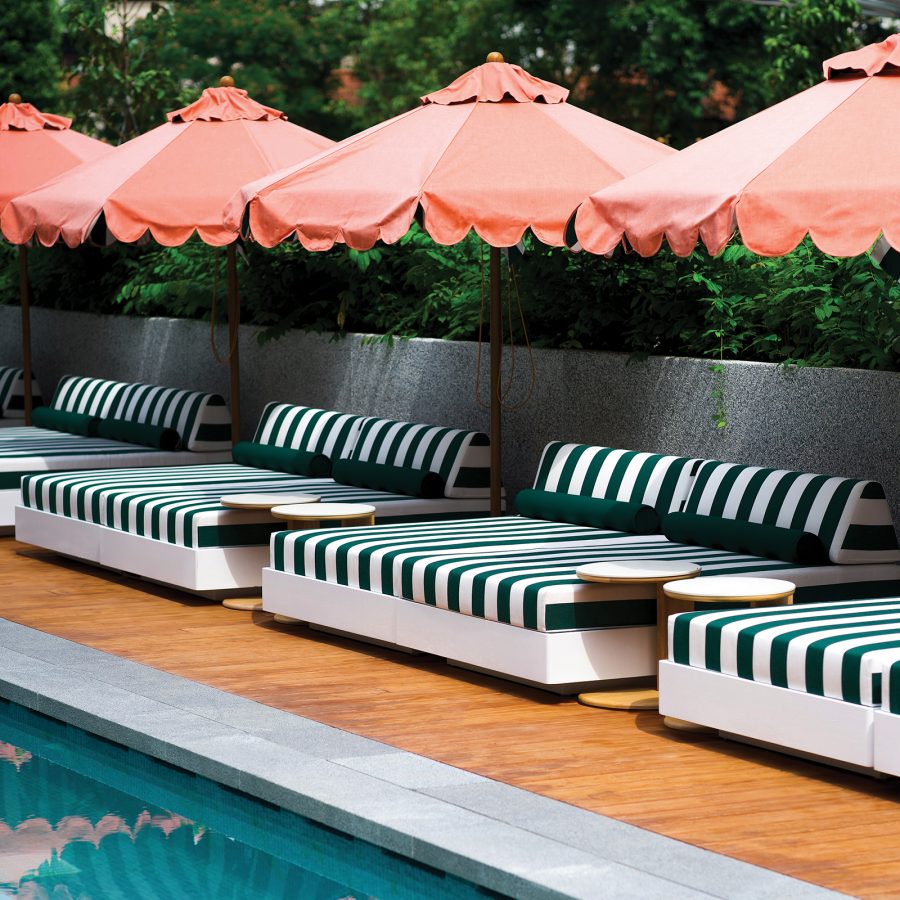 Green striped sunbeds under peach umbrellas, poolside at The Standard, Singapore. 