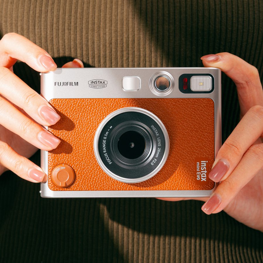  A person with painted brown nails holds the Fujifilm Instax Mini Evo against their chest.