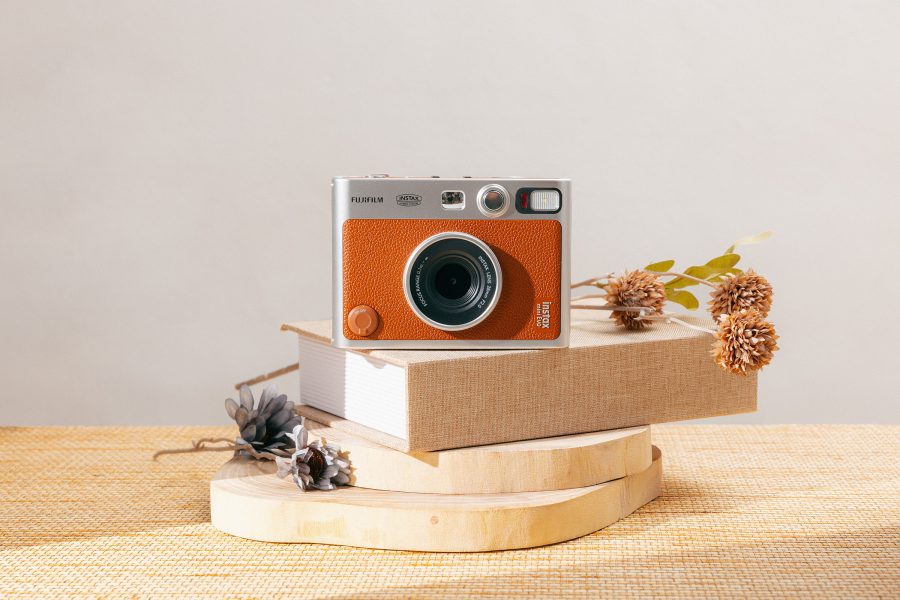 The Fujifilm Instax Mini Evo camera sitting on a beige book and wooden planks.
