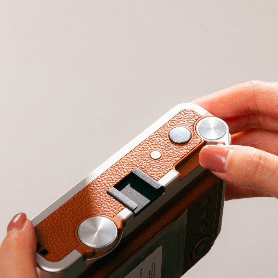 Person with painted brown nails twisting a dial on the Fujifilm Instax Mini Evo.