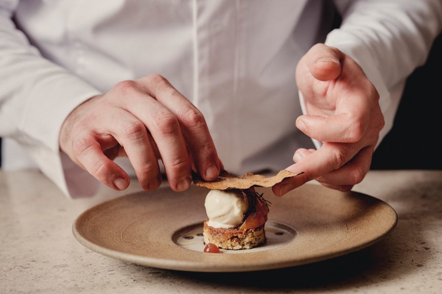 Closeup of chef��’s hands preparing an elegant dish on a earth-tone plate
