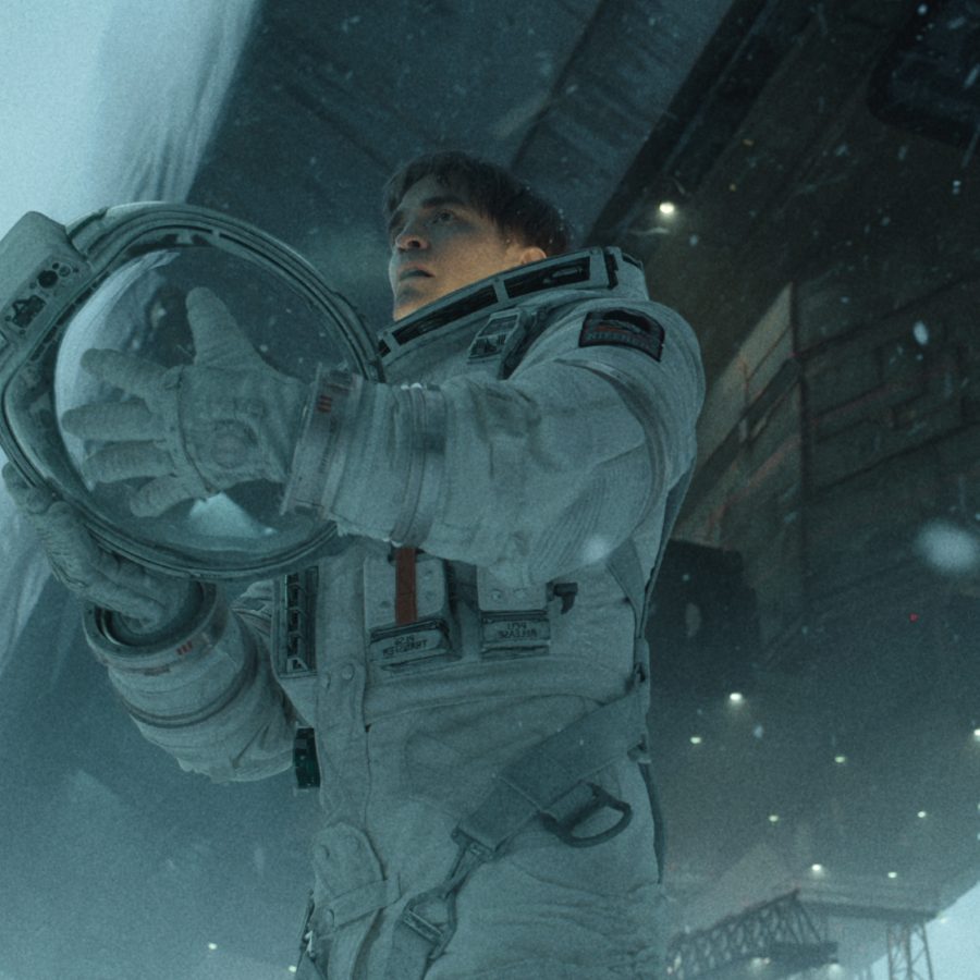 A man wearing an astronaut suit stand beneath a giant spacecraft in a scene from Mickey 17.