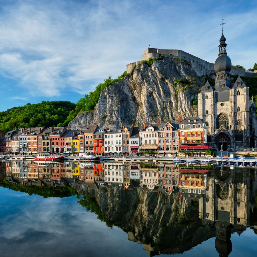 A view of Dinant shows colourful buildings at the foot of a dramatic cliff.  