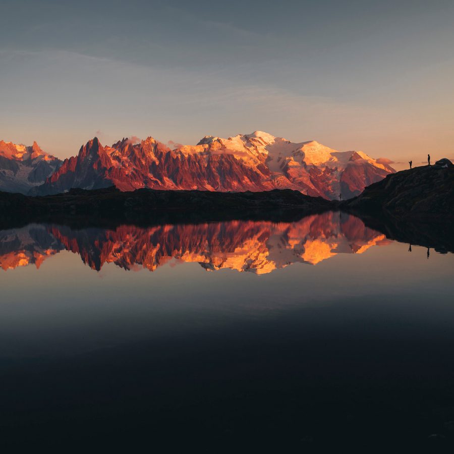 A view of the mountains from Chamonix shows the range glowing red and purple in the sunset and reflecting off the surface of a lake.
