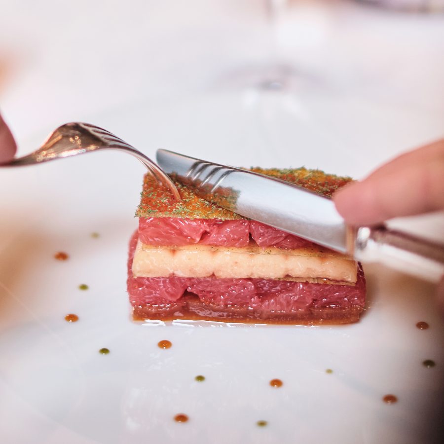 A person uses their knife and fork to dig into a delicately layered dish at Le Cinq in Paris. 