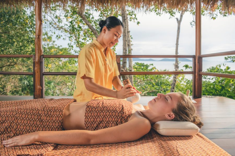  A woman lies on a massage table while a massage therapist conducts a spa treatment at Kamalaya Koh Samui.