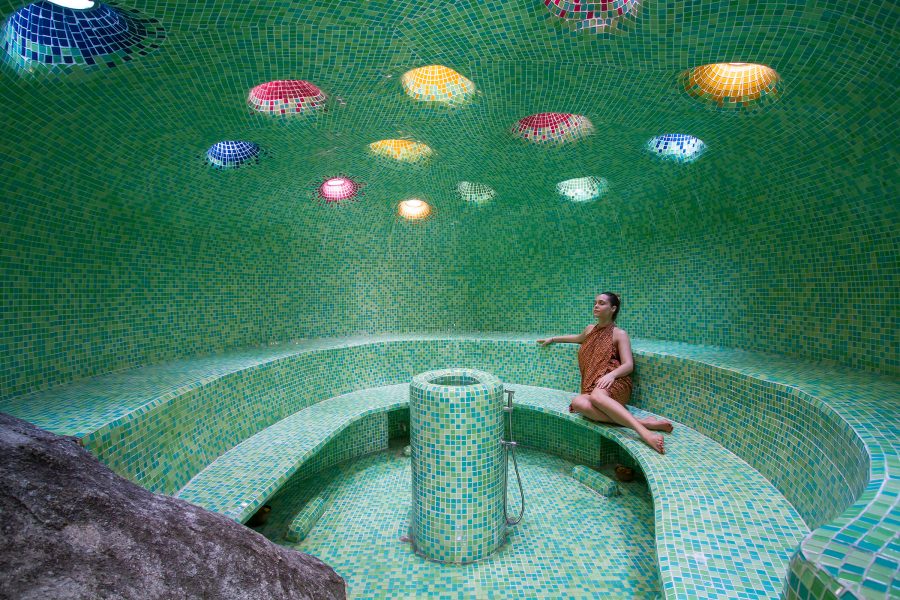 A woman relaxes in a green mosaic-tiled steam room at Kamalaya Koh Samui. 