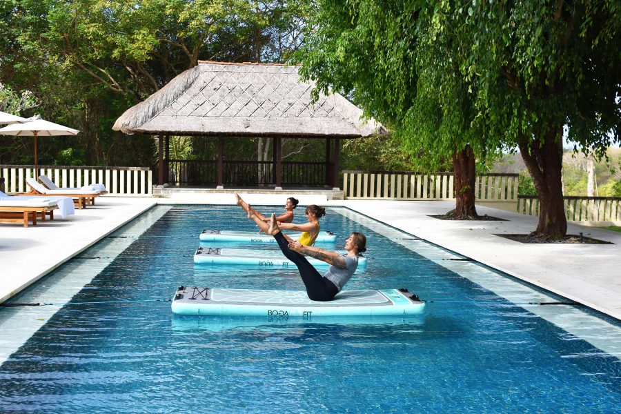 Three women practicing yoga on floating platforms in the pool at Revīvō Wellness Resort, Bali.