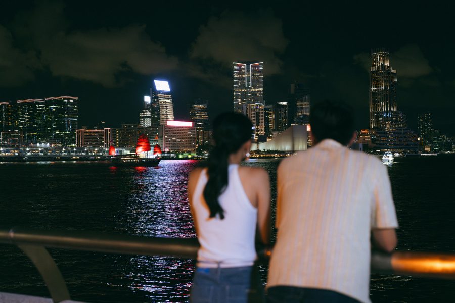 Two people leaning over a railing watching the Aqualuna junk sail through Victoria Harbour in Hong Kong.