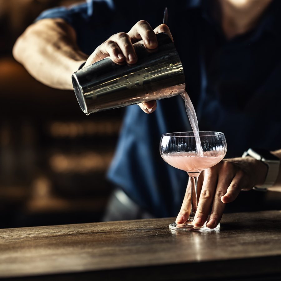 A person pouring a cocktail on a dark wood counter.