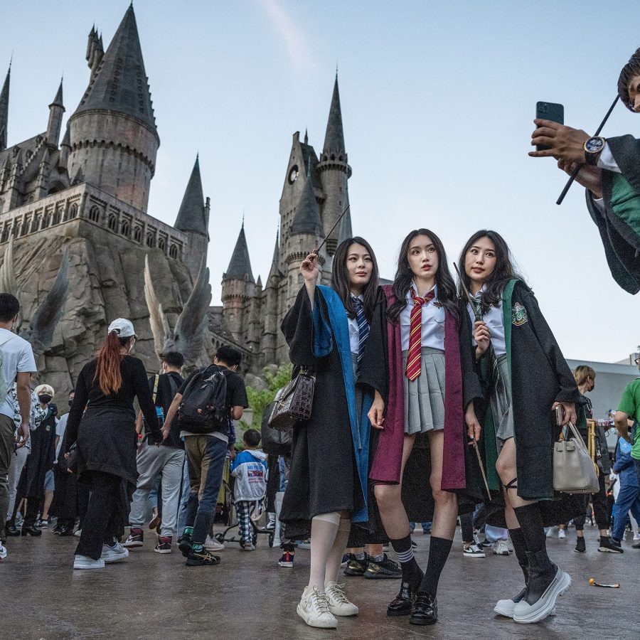 A group of friends wearing Harry Potter costumes taking photos with a view of a castle and crowd walking in the backdrop at Universal Beijing Resort, Beijing, China