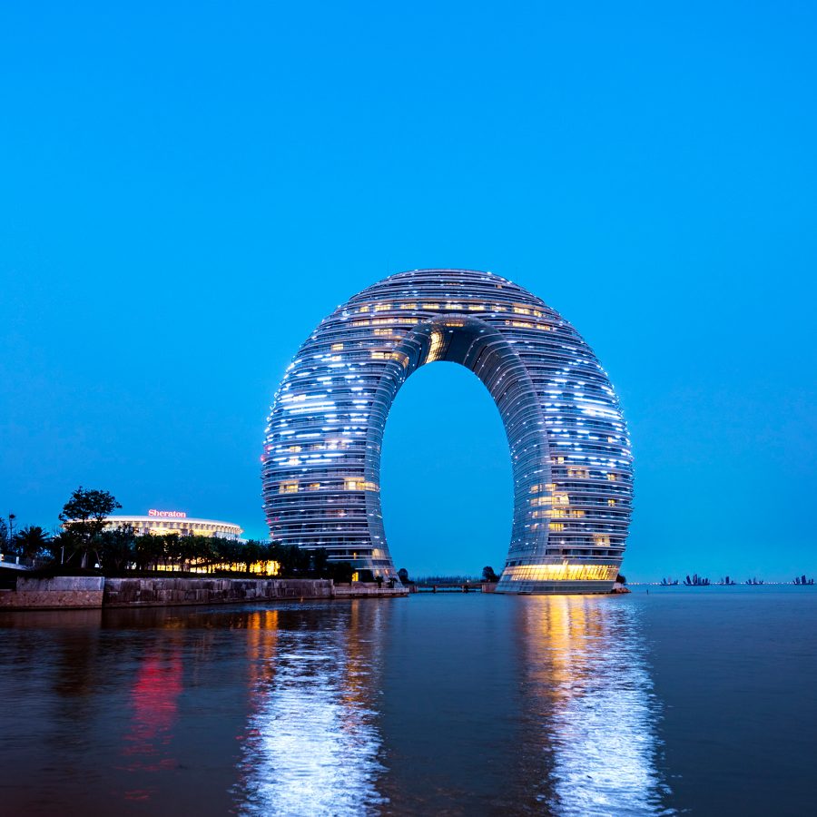 An evening view of Sheraton Huzhou Taihu Lake Hot Spring Resort & Spa lit up with a a Sheraton logo on its facade, overlooking Lake Taihu in Huzhou, China