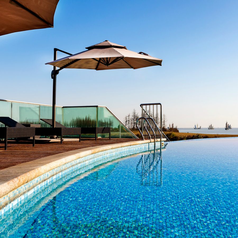 A view of the outdoor swimming pool with lounge furniture and sun umbrella at Sheraton Huzhou Taihu Lake Hot Spring Resort & Spa on a sunny day 