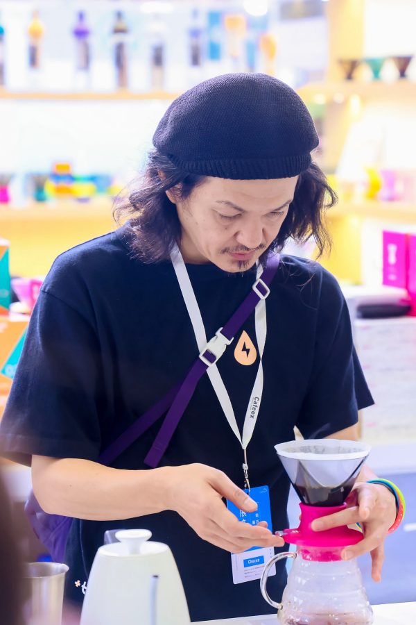 A man wearing a beret demonstrates how to use a pink pourover coffee device at the CAFEEX expo in Shenzhen.