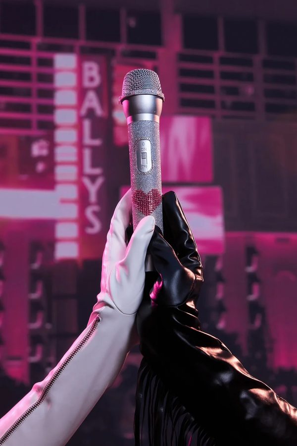 A person wearing a white glove holds up a silver microphone with a heart on it.