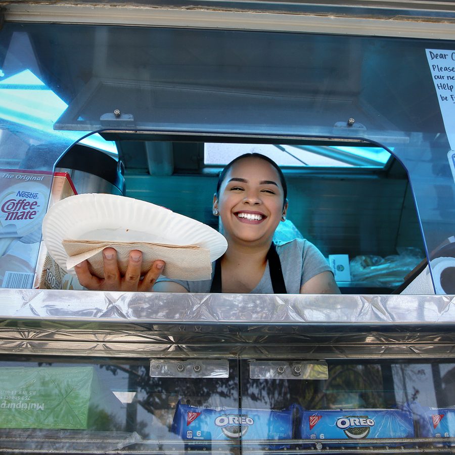 A woman smiling while holding a paper plate to a window at the El Gallo Giro foodtruck 