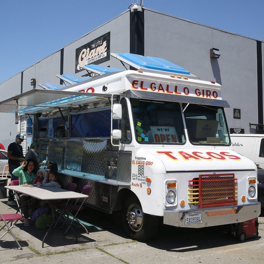 People lining up at El Gallo Giro food truck while people eat at a folding table in San Francisco