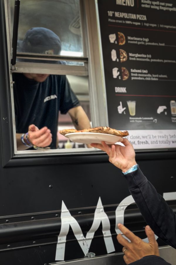A person handing a pizza on a paper plate to another person through the window of a food truck at Mozzeria in San Francisco 