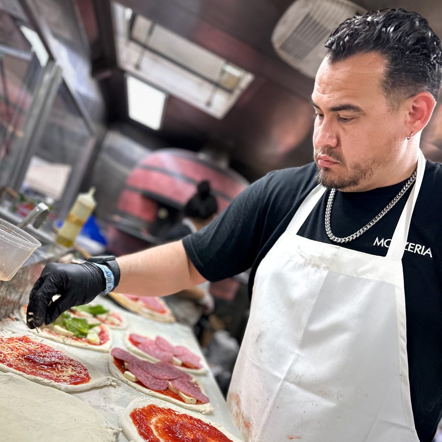 A closeup of a chef sprinkling cheese over pizza at Mozzeria in San Francisco