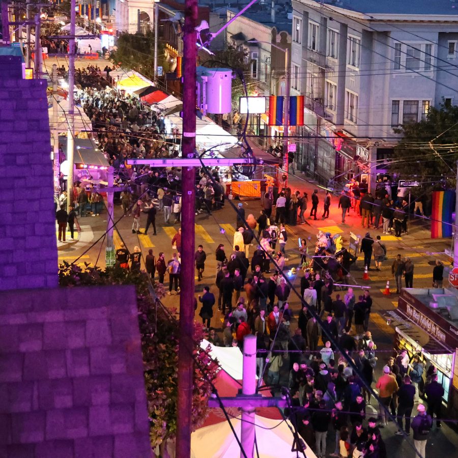 A crowd walking through San Francisco’s night market with food trucks parked along the sidewalk and vibrant lights illuminating the streets and houses