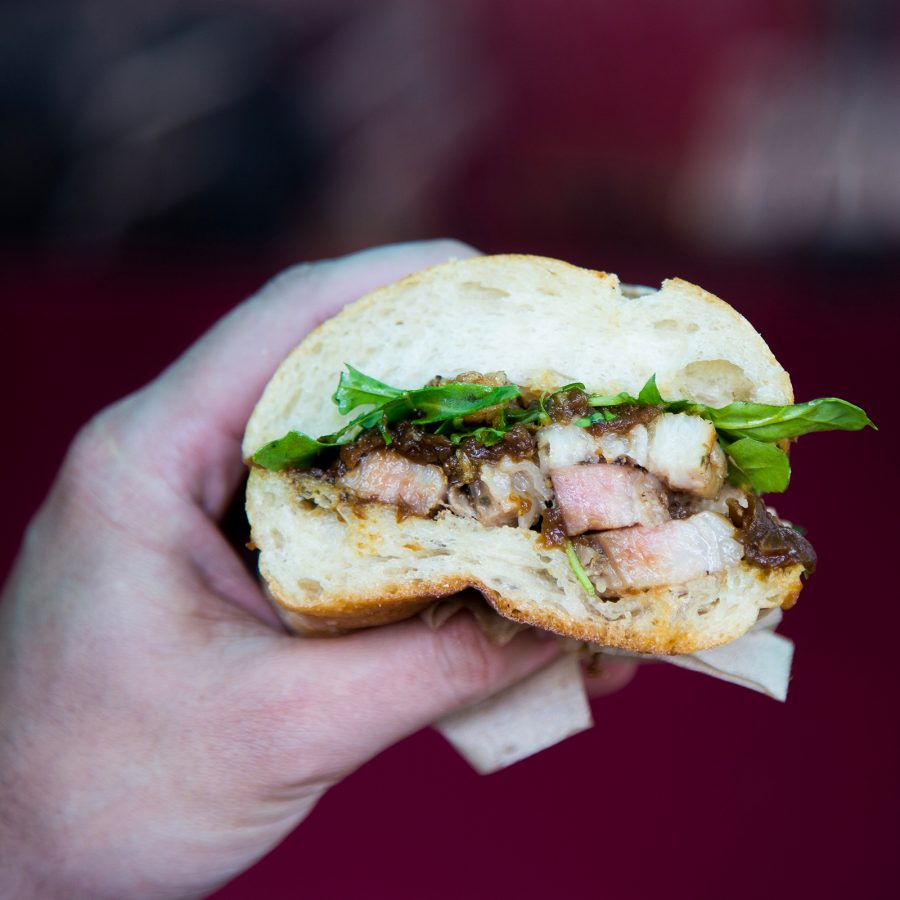 A hand holding up an openfaced porchetta sandwich, served at Roli Roti in San Francisco