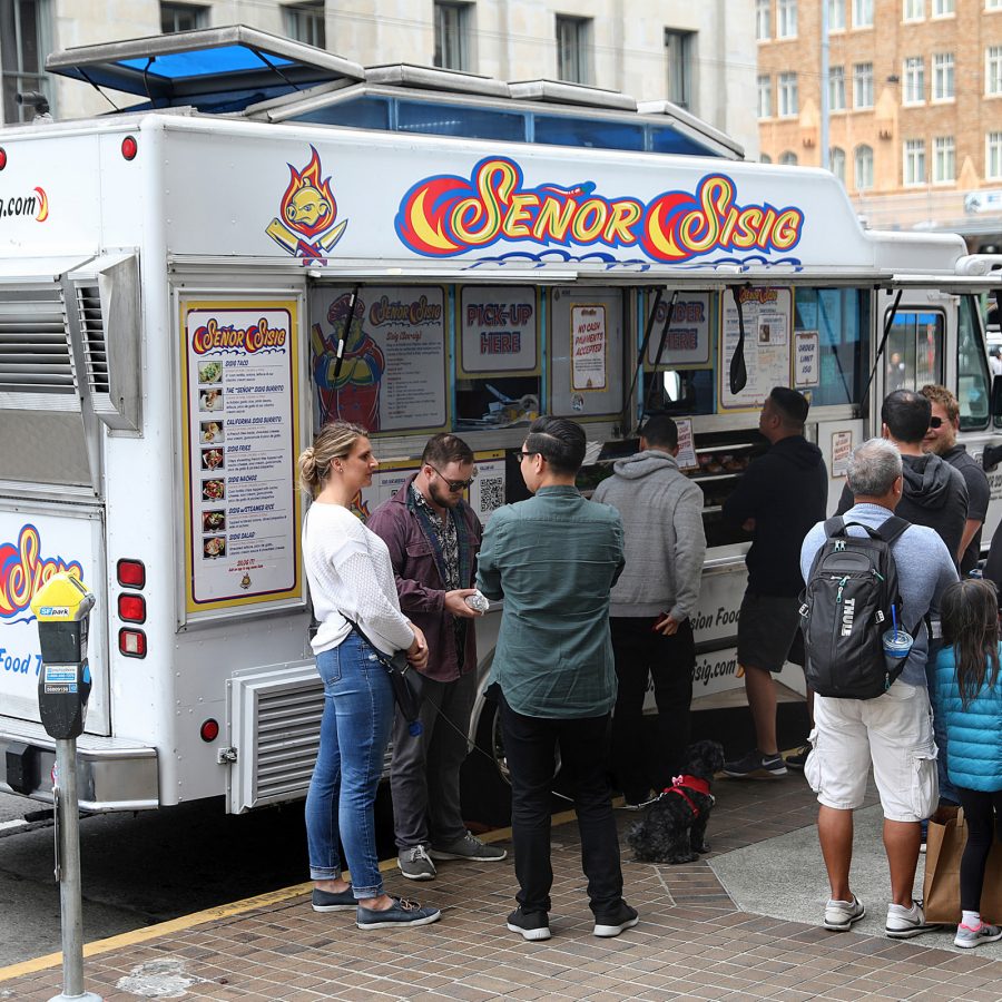 People crowd around Senor Sisig food truck parked by the sidewalk at San Francisco