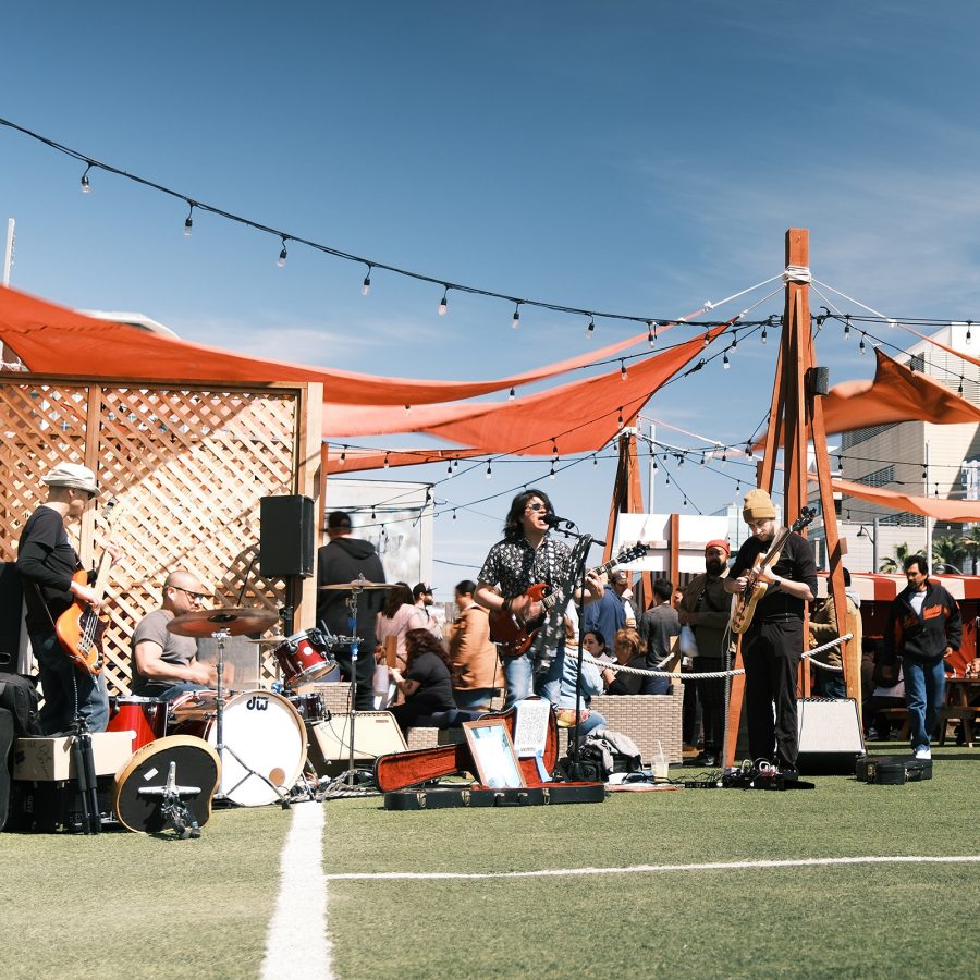A musical band playing on instruments under a canopy at food truck park Spark Social SF on a sunny day in San Francisco