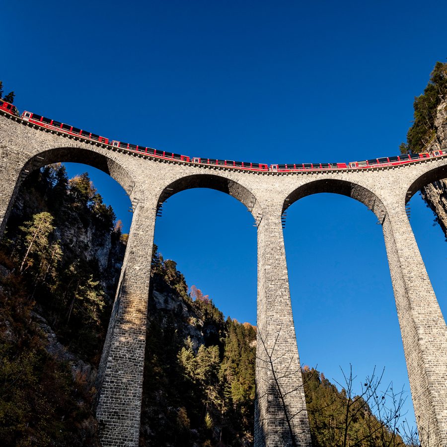 The Bernina Express travels between mountains connected by a bridge.