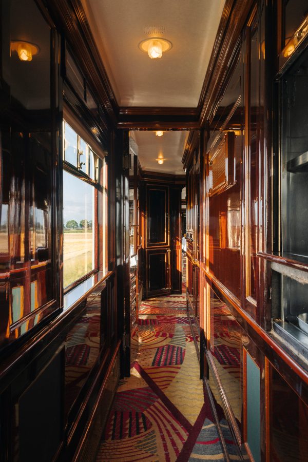 Varnished walls lining a narrow carpeted hallway on the Venice Simplon-Orient Express shine in the sunlight. 