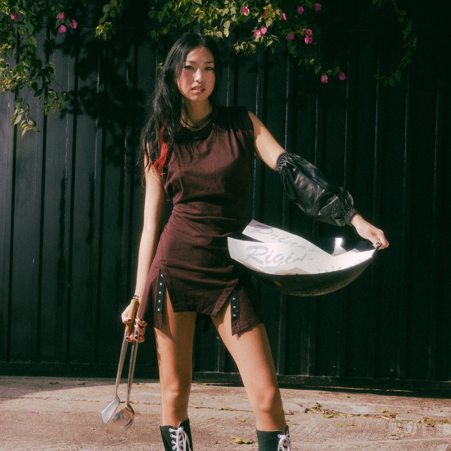Sam Lui from Wendy’s Wok World posing in a brown dress while holding a wok on her hip.