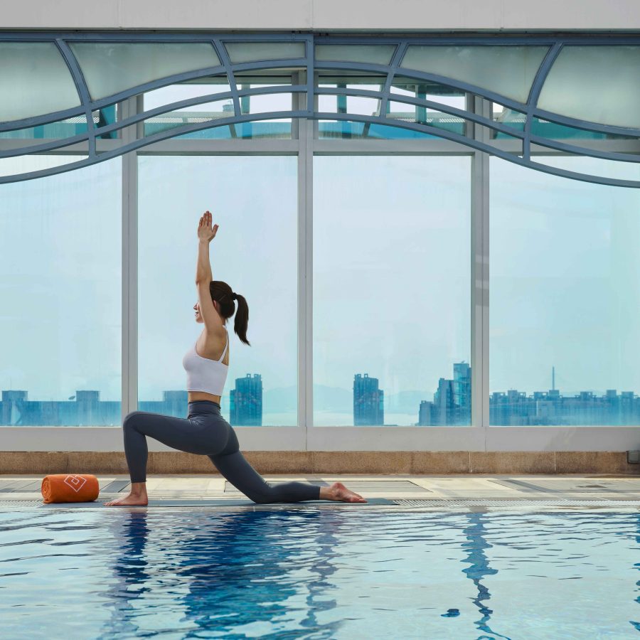 A person doing a yoga pose in front of the Hong Kong skyline in the Cordis pool