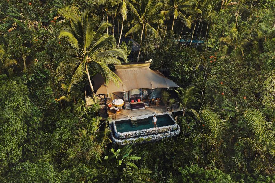 Aerial daytime view of a tented accommodation with an outdoor pool nestled in the forest at Capella Ubud, Bali.