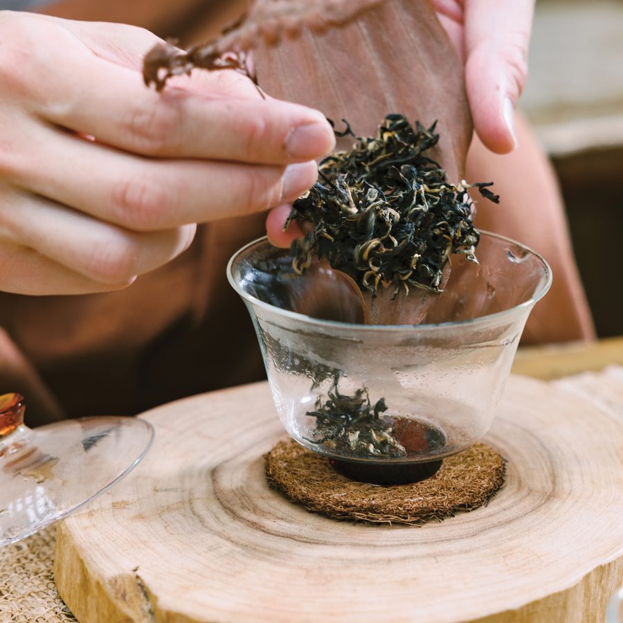 Person filling glassware with tea leaves on a wooden block