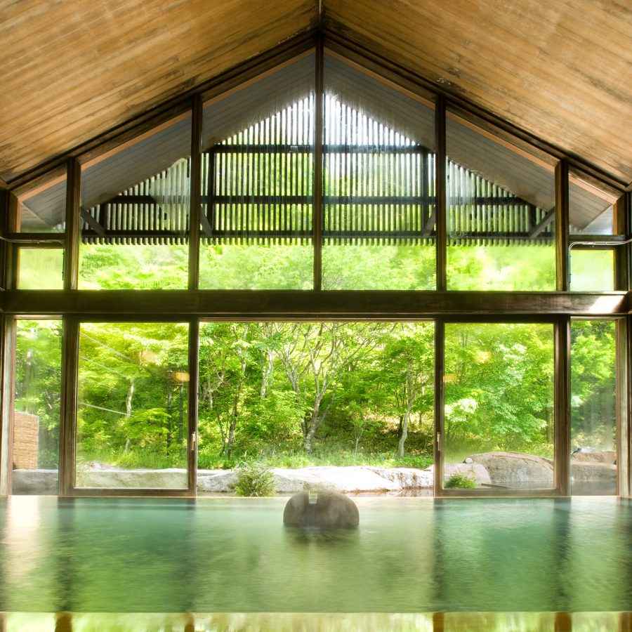 An indoor-outdoor water onsen at Hoshinoya Karuizawa with views out onto the forest beyond.