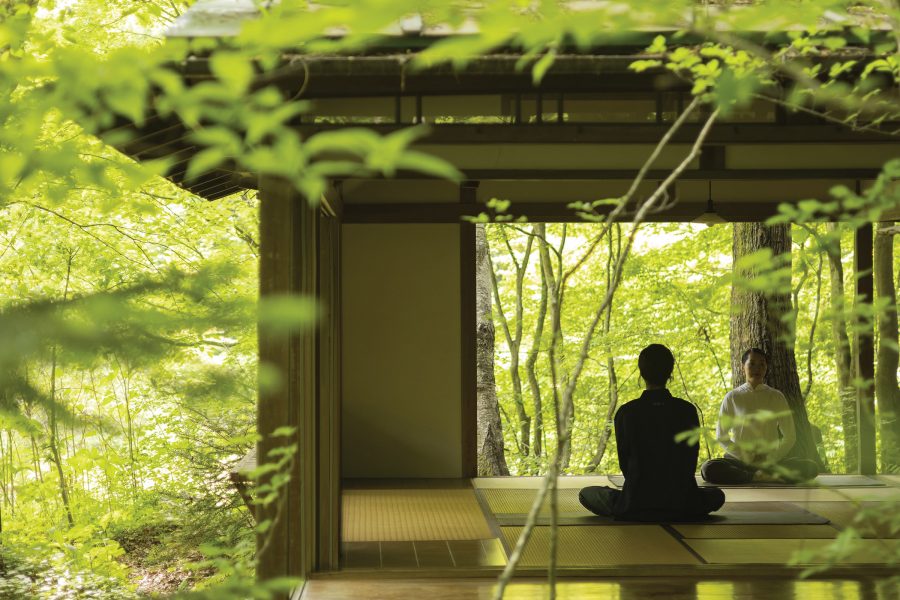 A person taking a meditation class sits in a tatami-floored building in the middle of a Japanese forest at Hoshinoya Karuizawa.