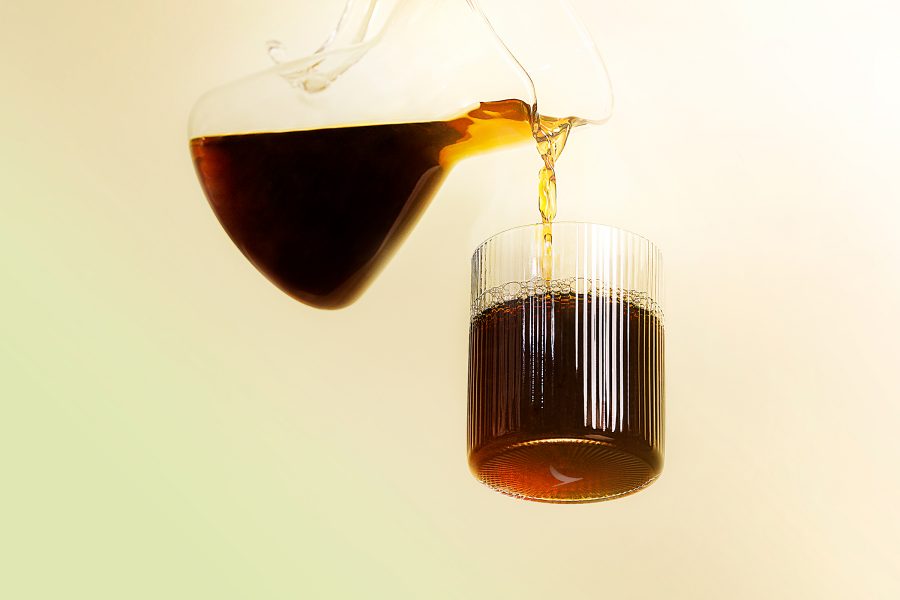 Coffee pours from a glass pitcher into a cup.