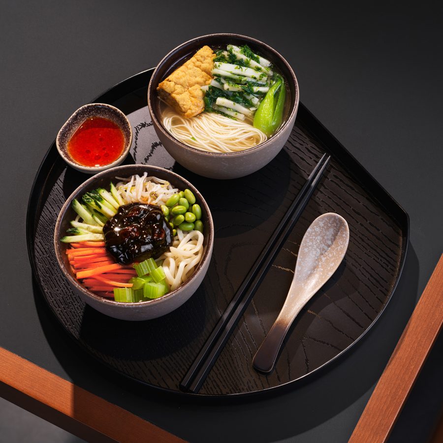 Two bowls of food with a side of sauce and utensils at the Beijing Cathay Pacific lounge.