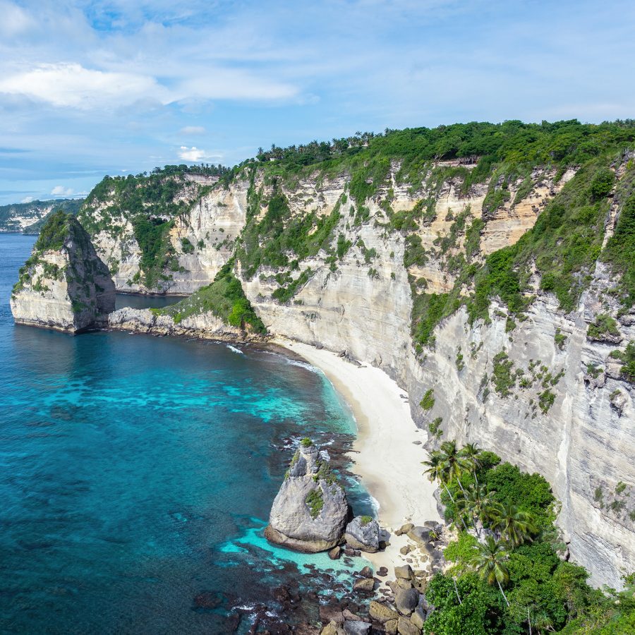 Cliffs draped with greenery rise above the water, forming Nusa Penida.