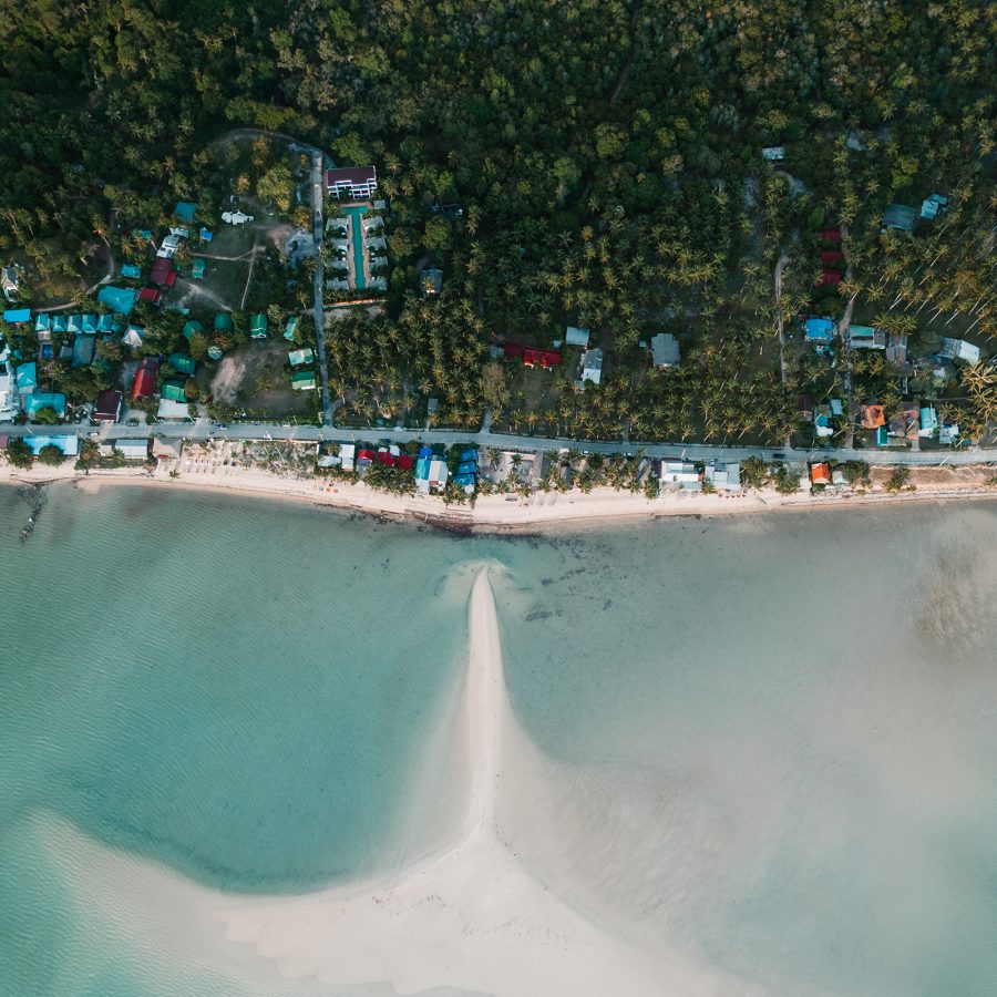 An aerial view of the coastline of Phuket shows a straight path next to a beach.