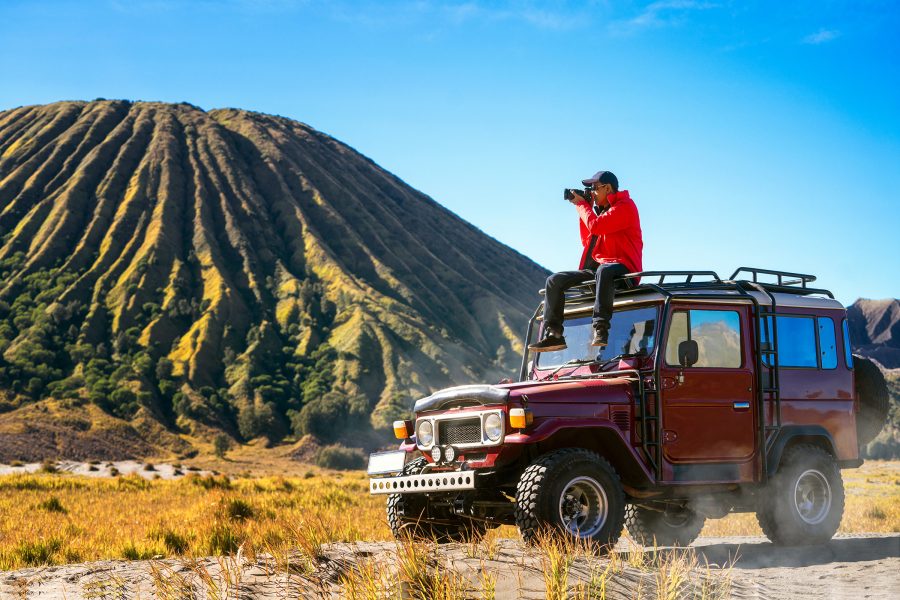 A photographer sits atop a jeep and takes a picture of the landscape while Mount Bromo in Surabaya appears in the background.
