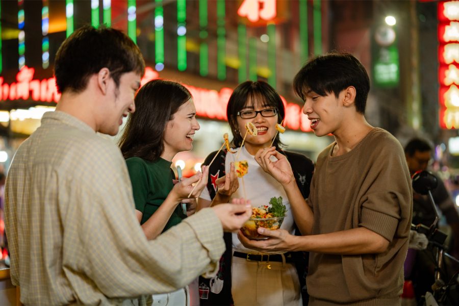 Four friends standing together sharing a bowl of food. 